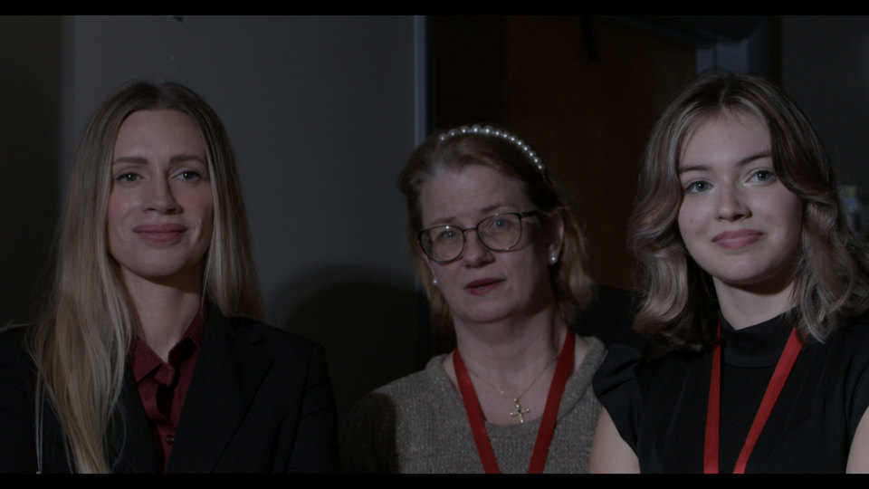 Three women stand together, red lanyards on